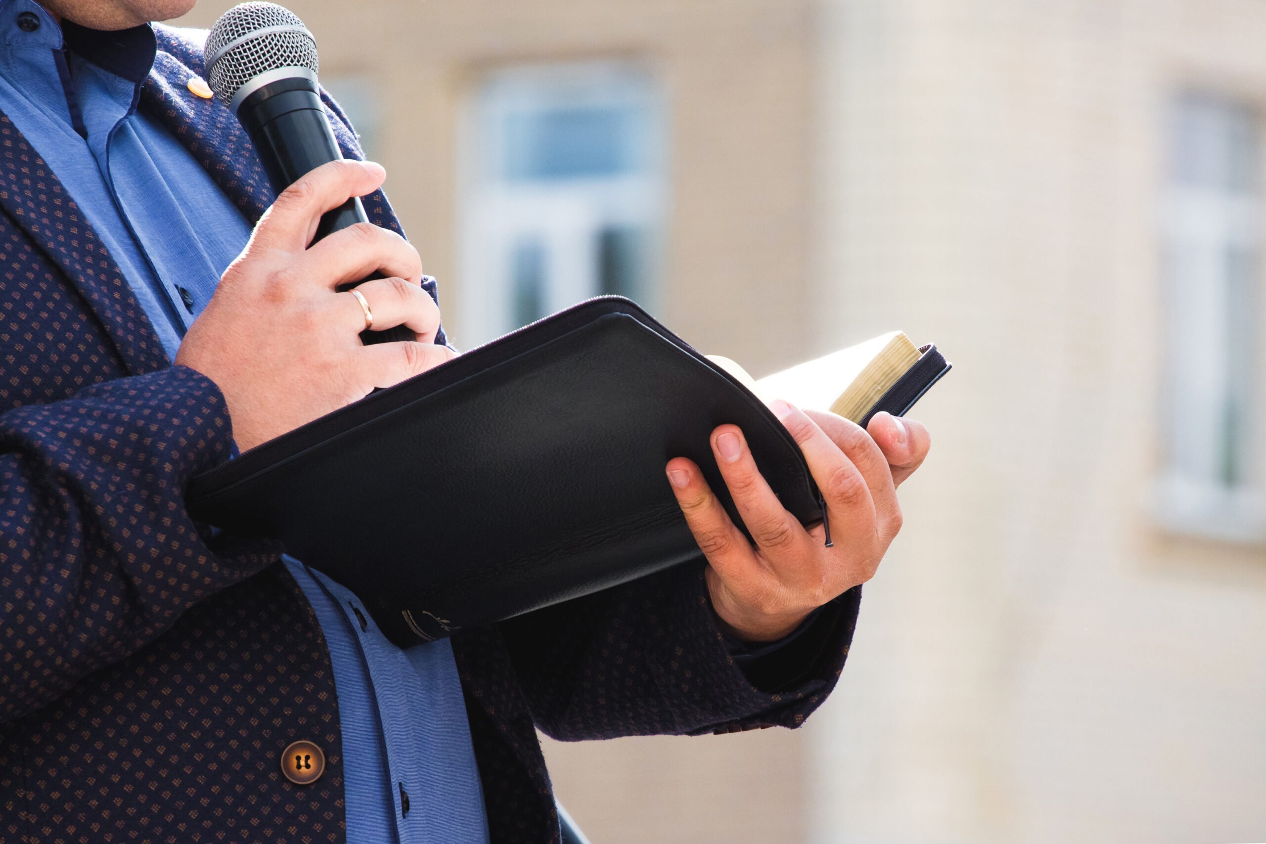 A preacher with a microphone in his hand holds a Bible and reads a passage from it