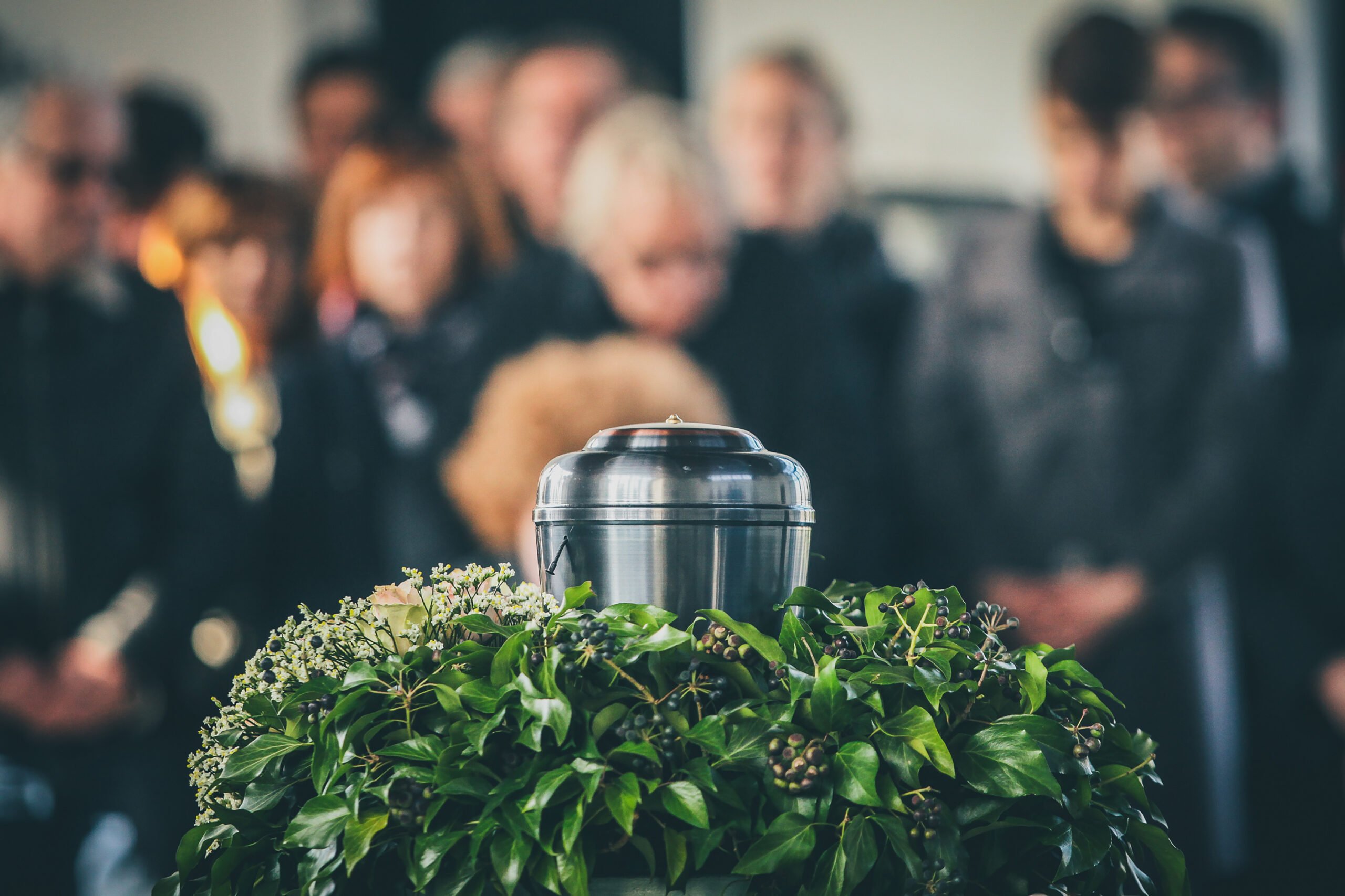 A metal urn with ashes of a dead person on a funeral, with people mourning in the background on a memorial service. Sad grieving moment at the end of a life. Last farewell to a person in an urn.