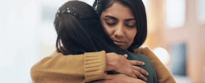 Two people embracing, with one woman comforting the other in a supportive hug.